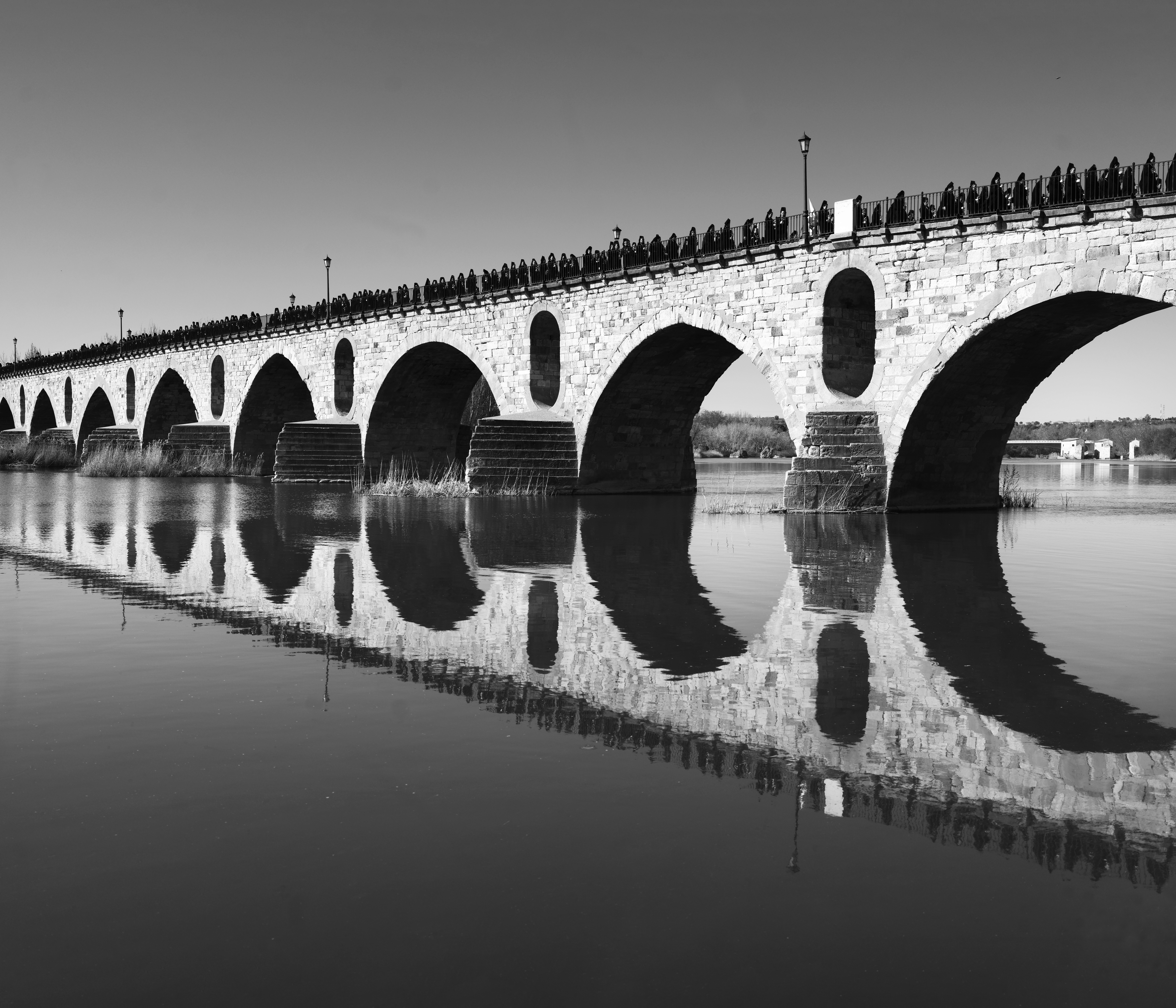 Una imagen en blanco y negro del Puente de Piedra de Zamora con el reflejo de la Semana Santa sobre el Duero, ganadora del VIII Concurso Fotográfico de la CHD